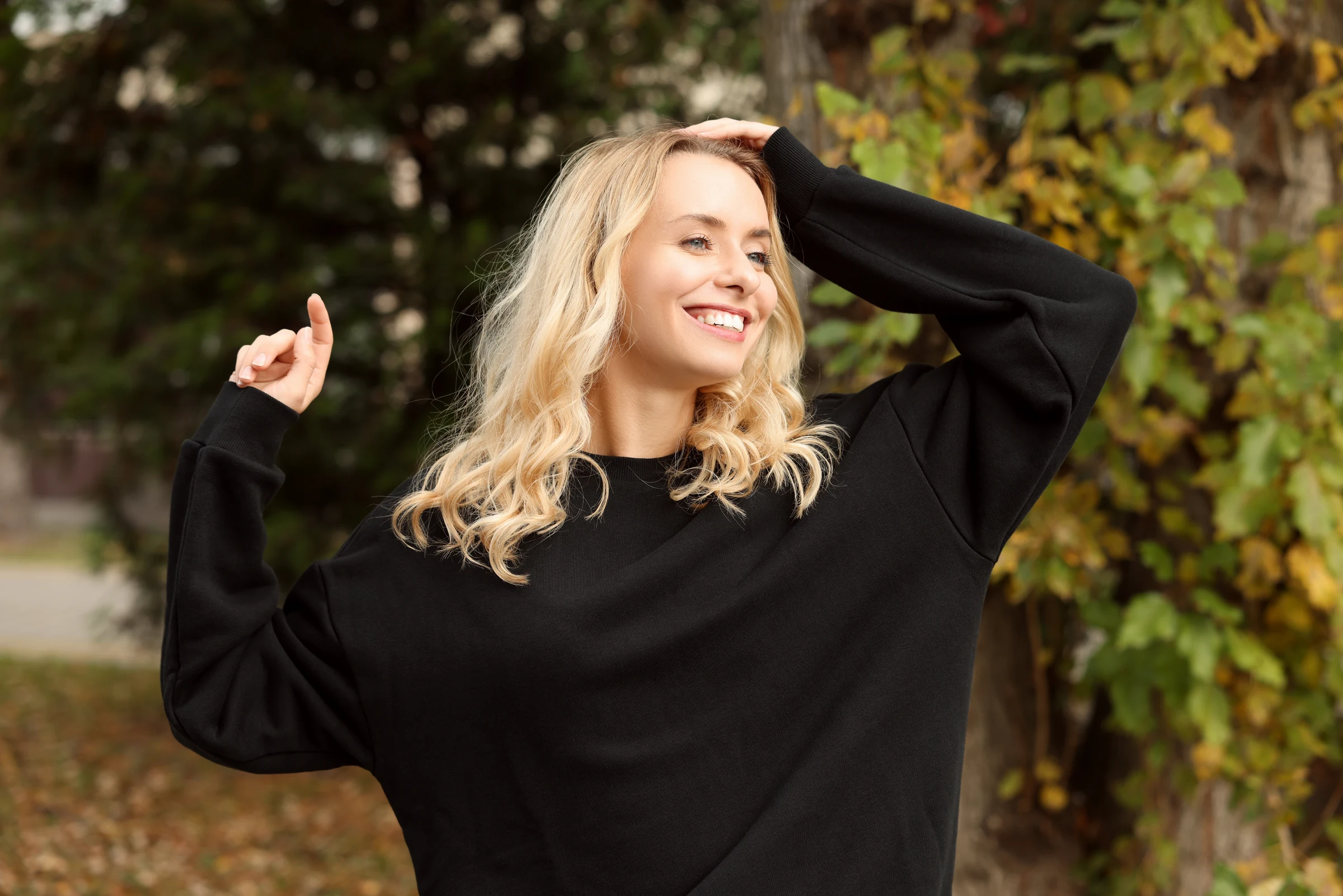 Blonde woman smiling outdoors with her hand in her hair